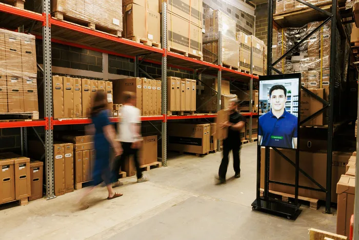 A RAVO kiosk in a busy warehouse aisle, visitors passing by